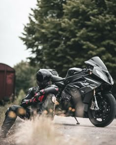 a person sitting on the ground next to a motorcycle in front of some trees and bushes