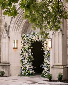 an archway decorated with flowers and greenery in front of a stone church entrance at night