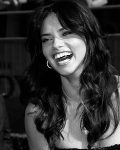 a woman with long hair laughing and wearing a strapless dress in front of a crowd