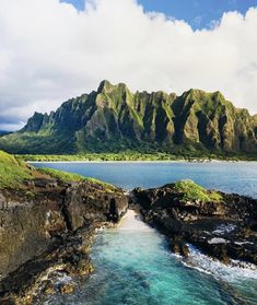 the ocean is clear and blue with green mountains in the backgroung area