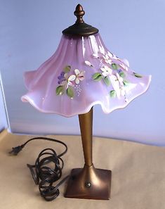 a pink lamp with flowers on it sitting on a table next to a charger