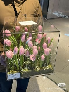 a man is holding a glass box with pink tulips and baby's breath