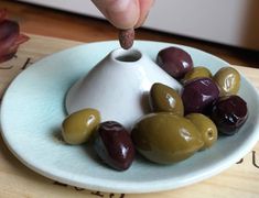 a hand is picking up some olives from a plate