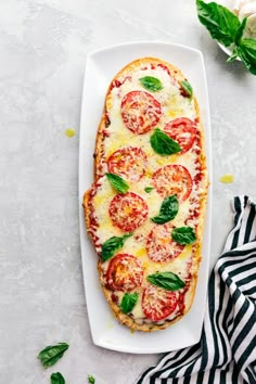 someone pointing at a pizza on a white platter with tomatoes and basil toppings