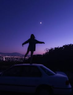 a woman standing on top of a car in the dark with her arms spread out