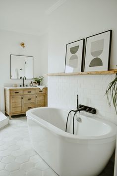 a large white bath tub sitting next to a sink in a bathroom under two framed pictures