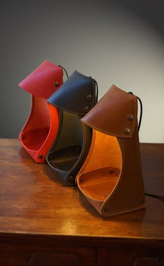 four different colored leather purses sitting on top of a wooden table next to each other