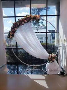 a wedding arch decorated with flowers and white draping in front of a window