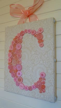 the letter c is made out of buttons and pink ribbon on a white wall with an orange bow