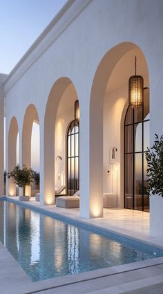 an outdoor swimming pool surrounded by arches and windows at dusk with lights on the side