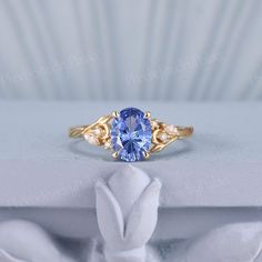 a ring with a blue stone in the center and two diamonds on each side, sitting on top of a white box