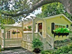 a small yellow house with potted plants on the porch