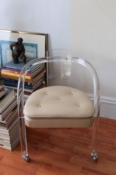 a clear chair sitting on top of a wooden floor next to a pile of books