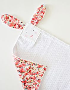 an oven mitt with flowers on it sitting next to a white towel and bunny ears