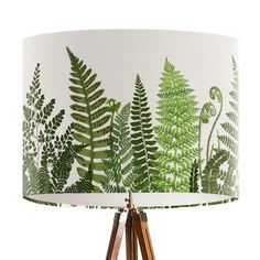 a lamp with a green fern print shade on it and wooden tripod lampshade