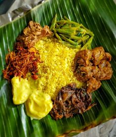 a large green plate topped with different types of food on top of a banana leaf