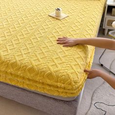 two hands reaching for a yellow bedspread on top of a bed in a bedroom