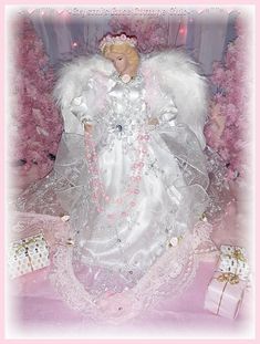 a white angel doll sitting on top of a pink blanket next to presents and trees