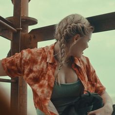 a woman standing in front of a wooden fence with her hand on her hip and looking at the sky