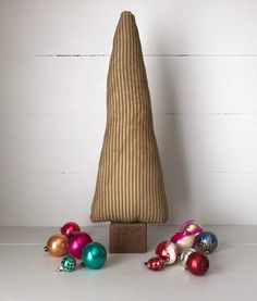 a small wooden christmas tree with ornaments around it on a white countertop next to a striped pillow