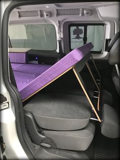 the back end of a vehicle with a purple bed in it's cargo area