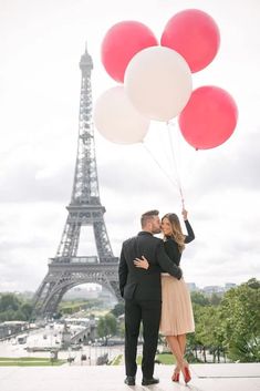 a man and woman standing in front of the eiffel tower with red and white balloons