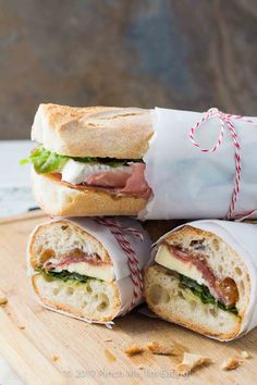 two sandwiches wrapped in paper sitting on top of a cutting board