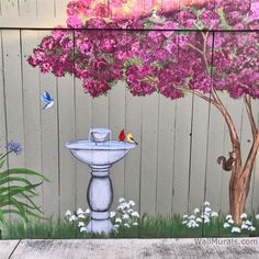 a painting on the side of a wooden fence with flowers and a bird bathtub