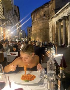 a woman sitting at a table eating spaghetti