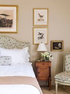 a bedroom with pictures on the wall above the bed and two chairs in front of it