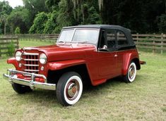 an old red and black car is parked on the grass in front of a fence