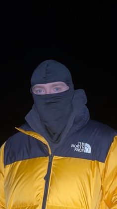 a man wearing a yellow and black jacket with a hood on, standing in the dark