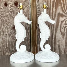 two white ceramic seahorses are standing next to each other on a wooden table