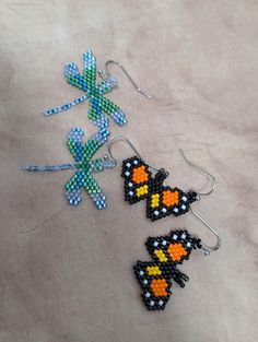 three beaded butterfly earrings are on the floor next to each other and one has an orange, yellow, blue, and black design