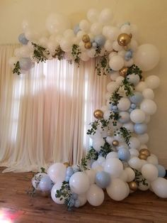 the balloon arch is decorated with greenery and white, blue and gold balloons for a party