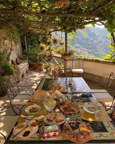 an outdoor table with food and drinks on it in front of a stone wall covered patio