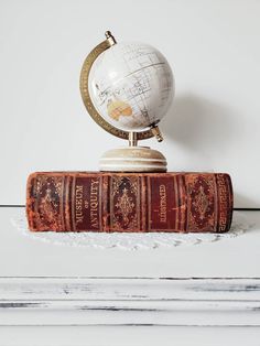 an old book sitting on top of a wooden table next to a small white globe