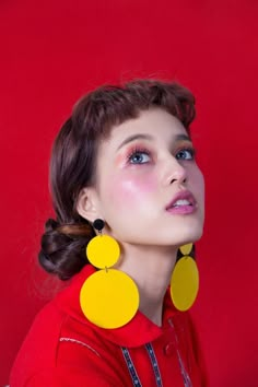 a woman wearing large yellow earrings and a red shirt is looking up at the sky