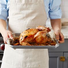 a person in an apron holding a roasting pan filled with chicken