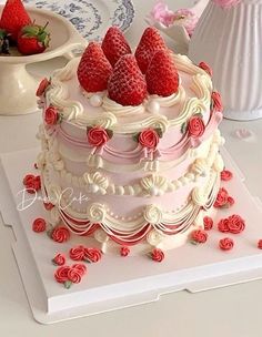 there is a large cake with strawberries on top and roses around the edges, sitting on a table