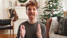 a man sitting in front of a christmas tree with his hands up to the camera