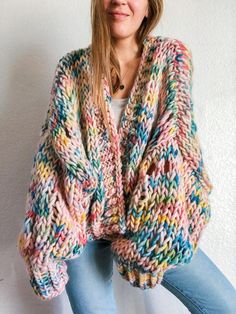 a woman is wearing a multicolored cardigan sweater and jeans, posing for the camera