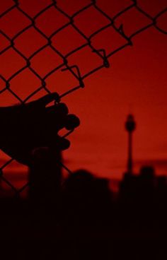 the silhouette of a person's hand holding onto a chain link fence at sunset