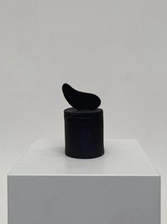 a black object sitting on top of a white block in front of a gray wall