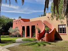 a pink house with plants in the front yard and palm trees on the other side