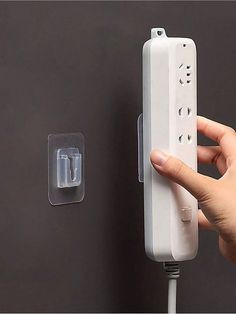 a person holding a wii remote in their hand next to a wall with two plugs on it