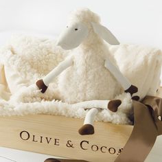 a stuffed sheep in a wooden crate with a brown ribbon around it's neck