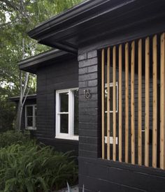 a small black house with wooden slats on the front door and side windows, along with succulents