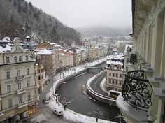 a river running through a city next to tall buildings covered in snow on a cloudy day