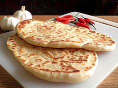 two flat breads sitting on top of a cutting board next to garlic and peppers